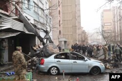 Military and onlookers stand at the site where a helicopter crashed near a kindergarten outside the capital Kyiv, killing eighteen people, including three children and the Ukrainian interior minister, on Jan. 18, 2023.
