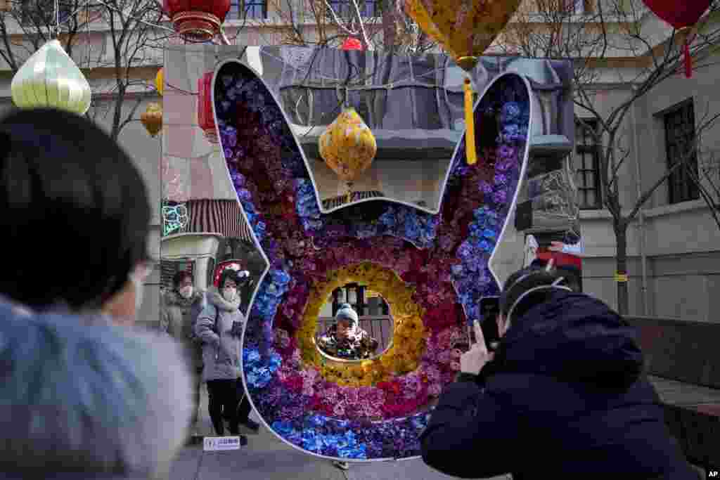 Un niño pequeño posa para una foto de recuerdo con una decoración floral en forma de conejo en una calle comercial peatonal en Qianmen, en Beijing.