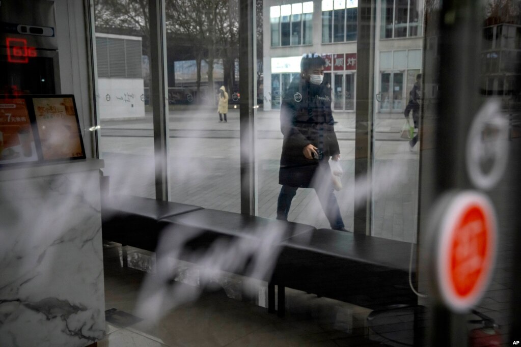 北京CBD金融区一家关门的商店外走过戴着口罩的行人。（2023年1月17日）(photo:VOA)