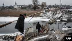 La gente camina sobre un puente destruido para cruzar un canal hacia el área en disputa en Bakhmut el 1 de febrero de 2023, en medio de la invasión rusa de Ucrania. (Foto de YASUYOSHI CHIBA / AFP)