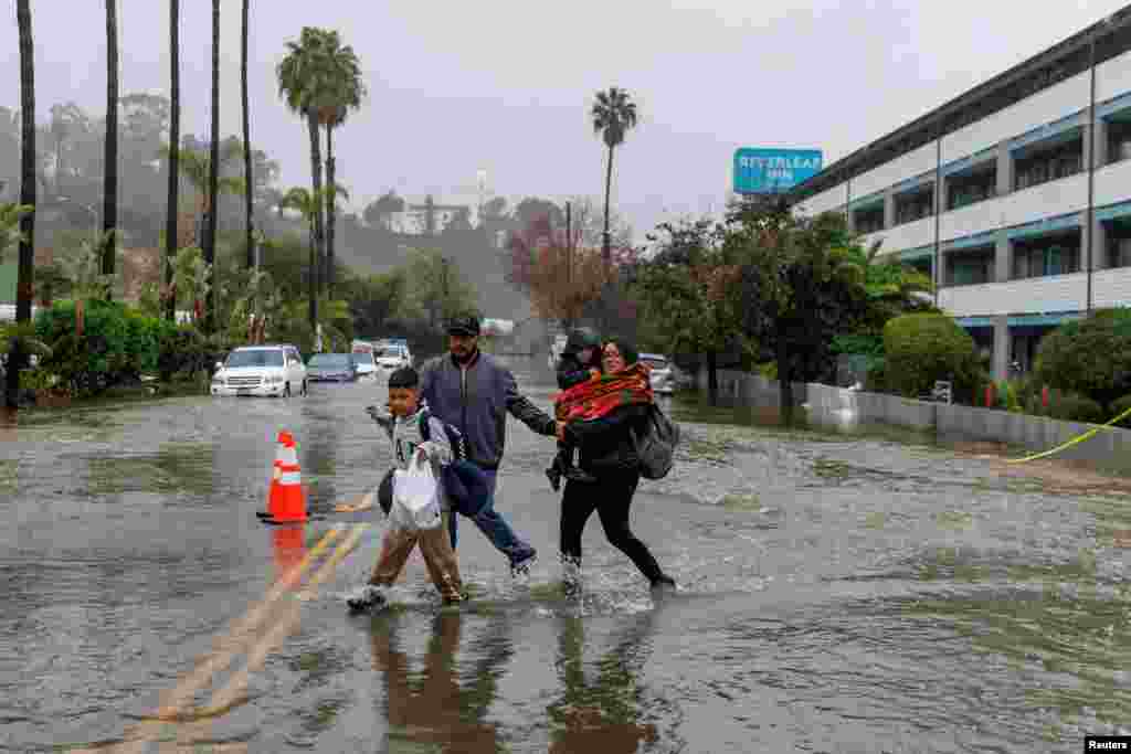 People cross a flooded street outside a hotel in San Diego, California, Jan. 16, 2023.