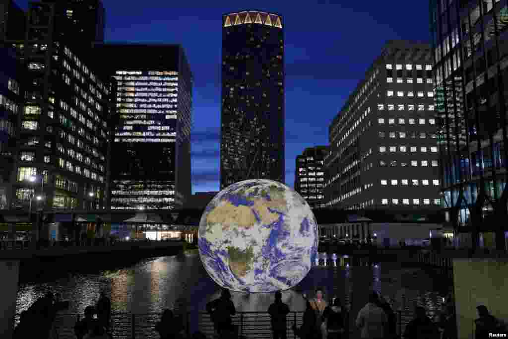 People look at Luke Jerram&#39;s &quot;Floating Earth,&quot; an installation as part of the Canary Wharf Winter Lights festival in the financial district in London, Jan. 17, 2023.