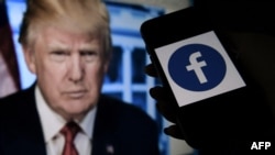 FILE - A phone screen displays a Facebook logo with the official portrait of former U.S. President Donald Trump in the background in Arlington, Va., May 4, 2021.