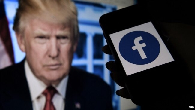 FILE - A phone screen displays a Facebook logo with the official portrait of former U.S. President Donald Trump in the background in Arlington, Va., May 4, 2021.