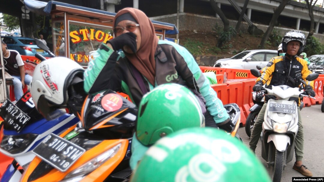 A GrabBike driver and an Uber driver wait on the pedestrians as they wait for customers in Jakarta, Indonesia (Achmad Ibrahim/AP)
