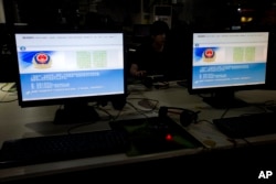 FILE - A computer user sits near displays with a message from the Chinese police on the proper use of the internet at an internet cafe in Beijing, China.