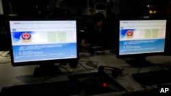 FILE - A computer user sits near displays with a message from the Chinese police on the proper use of the internet at an internet cafe in Beijing, China, Aug. 19, 2013.
