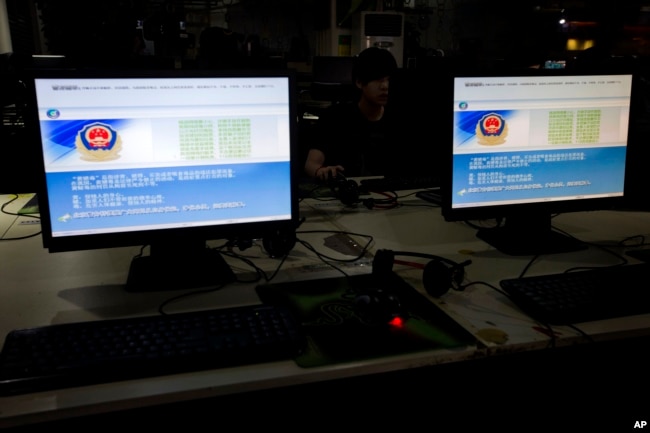 FILE - A computer user sits near displays with a message from the Chinese police on the proper use of the internet at an internet cafe in Beijing, China.