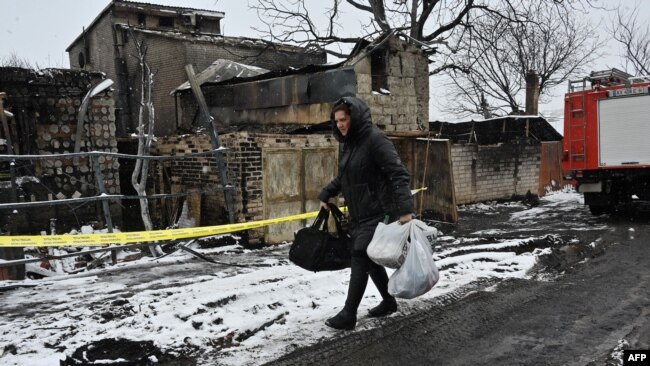 10 Şubat 2024 - Bir kadın, üçü çocuk yedi kişinin öldüğü insansız hava aracı saldırısında yanan bir konutun önünden yürüyerek geçiyor.