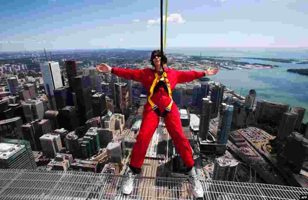 July 27: A reporter leans over the edge of the catwalk during the media preview for the "EdgeWalk" on the CN Tower in Toronto. Participants are strapped in to a harness that is attached to a guard rail while walking around the catwalk on the structure 356