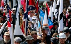 FILE - White nationalist demonstrators walk into Lee Park surrounded by counter demonstrators in Charlottesville, Va., Aug. 12, 2017.