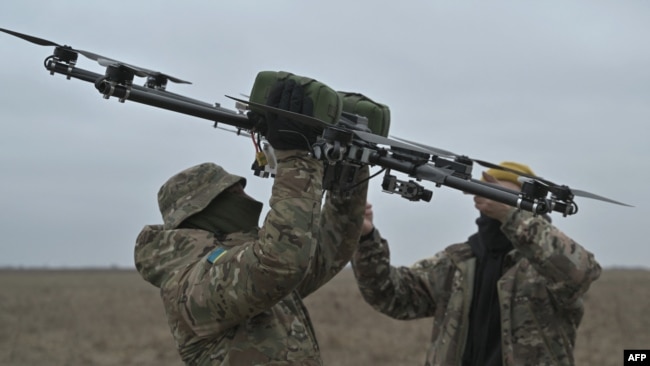 Оператори дрона несуть безпілотник на тренувальному полігоні в Київській області, 23 лютого 2024 року