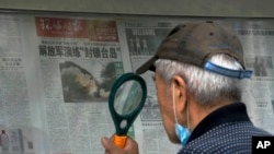 A man uses a magnifying glass to read a newspaper headline reporting on Chinese People's Liberation Army (PLA) conducting military exercises, at a stand in Beijing, Aug. 7, 2022. 