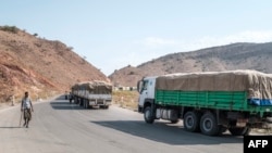 FILE - A man walks next to a convoy of trucks on their way to Tigray in the village of Erebti, Ethiopia, June 9, 2022. The peace deal recently announced by Addis and Mekele is supposed to open relief corridors to get more into that starving, wounded region.
