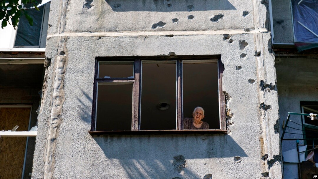 Seorang perempuan melongok ke luar jendela apartemennya di sebuah bangunan yang rusak akibat serangan roket pada Mei lalu, di Sloviansk, wilayah Donetsk, timur Ukraina, Sabtu, 6 Agustus 2022.