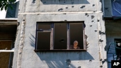 An elderly woman looks out of her apartment window in a building damaged in a May rocket attack in Sloviansk, Donetsk region, eastern Ukraine, Aug. 6, 2022.