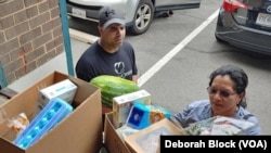 Leo Delgado, warehouse manager for Food for Others in Fairfax, Virginia, helps Maria Aguilar take food to her car. In addition to food, a local grocery store also donated flowers. (Deborah Block/VOA)