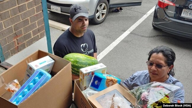 Leo Delgado, warehouse manager for Food for Others in Fairfax, Virginia, helps Maria Aguilar take food to her car. In addition to food, a local grocery store also donated flowers. (Deborah Block/VOA)