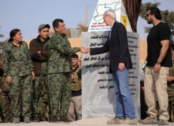 FILE - Mazloum Kobani, SDF's commander in chief, shakes hands with the advisor for the U.S. Department of State in northern Syria William Robak, at al-Omar oil field in Deir Al Zor, Syria, March 23, 2019.