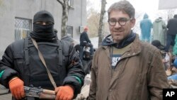In this photo taken on April 13, 2014, American reporter Simon Ostrovsky, right, stands with a pro-Russian gunman near a police station in the eastern Ukrainian town of Slovyansk. 