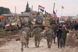 In this frame grab from video, Russian, Syrian and others gather next to an American military convoy stuck in the village of Khirbet Ammu, east of Qamishli city, Syria, Feb. 12, 2020.