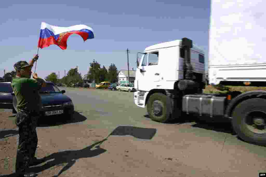 A local resident holds a Russian national flag as lorries, part of a Russian humanitarian convoy cross the Ukrainian border at the Izvarino custom control checkpoint, on Aug. 22, 2014. 