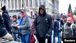 A man (center in black coat) identified by U.S. federal prosecutors as Shane Jason Woods of Auburn, Illinois. is seen in a frame grab from video shot during the Jan. 6, 2021 assault on the U.S. Capitol, moments before attacking members of the news media. 