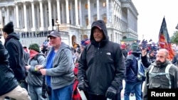 A man (center in black coat) identified by U.S. federal prosecutors as Shane Jason Woods of Auburn, Illinois. is seen in a frame grab from video shot during the Jan. 6, 2021 assault on the U.S. Capitol, moments before attacking members of the news media. 