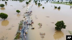 FILE - People walk through floodwaters after heavy rainfall in Hadeja, Nigeria, Monday, Sept 19, 2022.