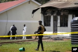 Security forces and forensics officers stand in front of a burned dormitory at the scene of a fire at the Salama School for the Blind in Luga village, Mukono district, Uganda, Oct. 25, 2022.
