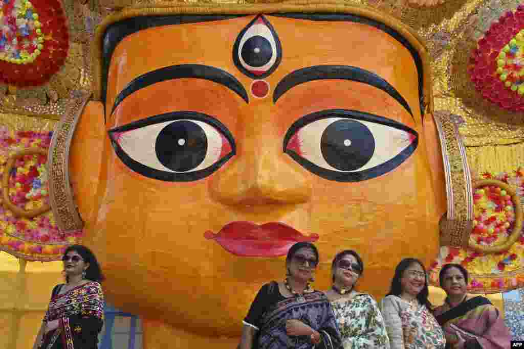 Visitors stand for pictures in front of a work of art next to a Durga Puja pandal in Kolkata, India.