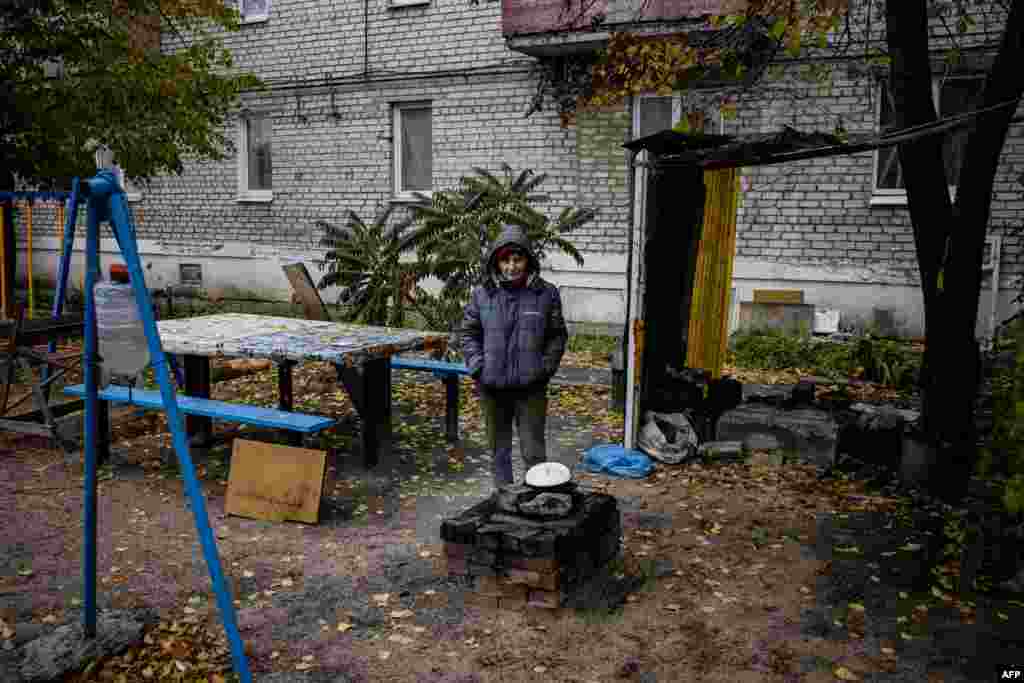 Tashqarida ovqat pishirayotgan ayol. Urush tufayli ba&#39;zi joylarda gaz, suv, elektr energiyasi ta&#39;minoti uzilgan. Liman, Donetsk.