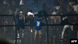 Para penonton memanjat pagar di dekat tribun penonton di tengah desak-desakan maut usai pertandingan sepak bola antara Arema FC dan Persebaya di stadion Kanjuruhan di Malang, Jawa Timur (Foto: AFP)