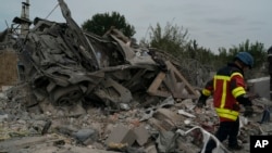 2022年10月9日，乌克兰扎波罗热，一名救援人员走过一辆撞毁的汽车，那里有几栋房屋在俄罗斯袭击后被毁。