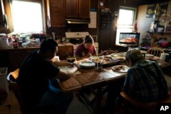 Molly Snell, center, says grace with her partner, Tyler Weyiouanna, foreground left, Weyiouanna's grandfather, Clifford, as they gather around a dinner table to celebrate Tyler's 31st birthday in Shishmaref, Alaska, Saturday, Oct. 1, 2022.