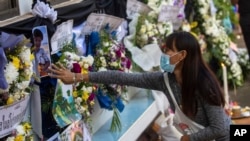 A woman touches a photo of the victims of a mass killing attack outside Wat Rat Samakee temple in Uthai Sawan, north eastern Thailand, Sunday, Oct. 9, 2022.