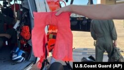 In this image provided by the U.S. Coast Guard, a Coast Guard Air Station New Orleans aircrew member holds up a life jacket from a recent rescue off the coast of Empire, La., on Oct. 9, 2022. The men said sharks shredded the life jacket.