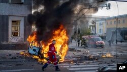 An emergency medical technician walks past a burning car after a Russian missile strike in Kyiv, Ukraine, Oct. 10, 2022. 