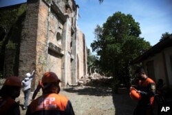 Petugas pemadam kebakaran berdiri di samping gereja yang rusak akibat gempa kuat di Ilocos Norte, Filipina Utara, Rabu 26 Oktober 2022. (AP)