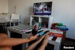 FILE - Ukrainian refugee Tatyana Bogkova talks on the phone with her husband, Andrey, with their daughter Eva as the TV in their flat in Madrid shows reports from Ukraine, Sept. 17, 2022.