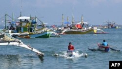 In this photo taken on August 20, 2022, crew on outriggers sail past fishing "mother" boats in the village of Cato, Infanta town, Pangasinan province, as they prepare to leave for a fishing expedition to the South China Sea.