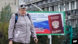 A woman walks past a billboard depicting Russian passport, a day after voting in four Moscow-held regions of Ukraine on referendums to become part of Russia, in Luhansk, Ukraine, Sept. 28, 2022.