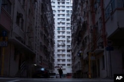 FILE - A man walks in front of a residential and commercial building, center, where "shoebox" apartments are located, in Hong Kong, April 25, 2017.