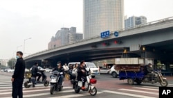 People ride scooters at an intersection near a bridge where social media videos earlier appeared to show smoke and protest banners in Beijing, Oct. 13, 2022. 