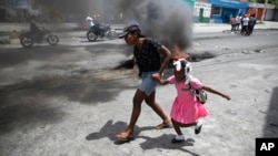 FILE - A woman guides a child past a demonstration against increasing violence in Port-au-Prince, Haiti, March 29, 2022.