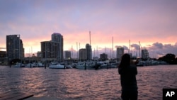 FILE - Kristi Burghdurf makes a photo of the sunset with her phone as an outer band of Hurricane Ian passes the waterfront of Tampa Bay, Sept. 27, 2022, in St. Petersburg, Fla.