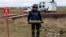 A Ukrainian service member holds a display munition during a mine-clearing demonstration with the Armtrac 400 demining machine in the background, in the Kharkiv region, Oct. 27, 2022. 