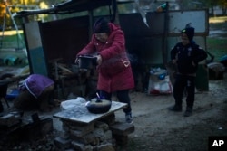 Iryna Panchenko removes a pot of food from a makeshift stove next to her grandchild Artem in Kivsharivka, Ukraine, Sunday, Oct. 16, 2022. (AP Photo/Francisco Seco)