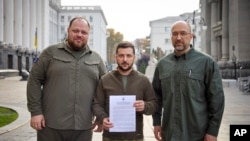 In a photo from Ukraine's Presidential Press Office, President Volodymyr Zelenskyy, center, with Prime Minister Denys Shmyhal, right, and head of the Supreme Council of Ukraine Ruslan Stefanchuk, holds an application for ''accelerated accession to NATO'' in Kyiv, Ukraine, Sept. 30, 2022.