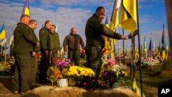 Ukrainian servicemen visit the grave of a recently killed fellow soldier, in a cemetery in Kharkiv, Oct. 14, 2022, as Ukraine marked Defenders Day.